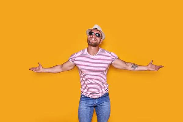 Sorprendido joven exitoso en gafas de sol y sombrero de paja de verano gritando con las manos abiertas sobre fondo amarillo — Foto de Stock