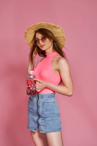 Cheerful beautiful beach girl in summer hat and sunglasses posing in body swimsuit, with cocktail in hand — Stock fotografie
