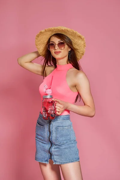 Cheerful beautiful beach girl in summer hat and sunglasses posing in body swimsuit, with cocktail in hand — Stock fotografie