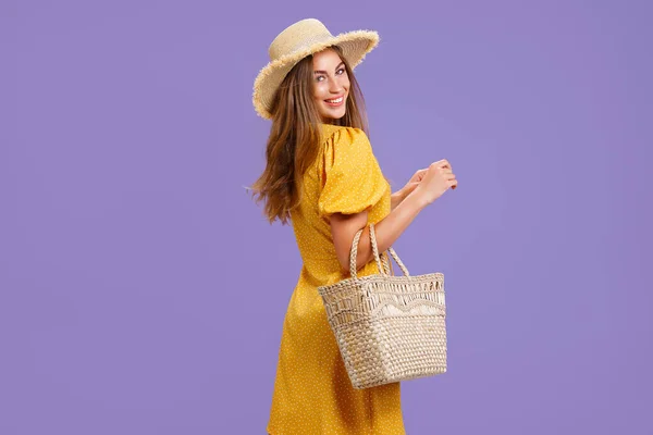 穿着黄色衣服、戴着夏草帽、头戴紫罗兰色背景的漂亮微笑的年轻女子. — 图库照片