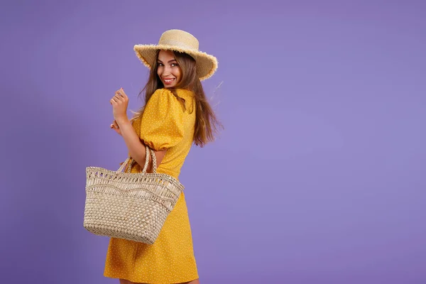 Bonita jovem sorridente em vestido amarelo, chapéu de palha de verão, saco isolado em fundo violeta pastel. — Fotografia de Stock