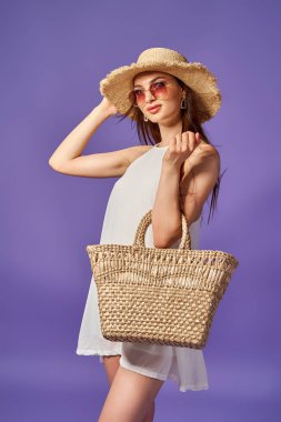 Beyaz elbiseli güzel bir kadın, yaz şapkası, pastel menekşe arka planda izole edilmiş bir çanta.. 