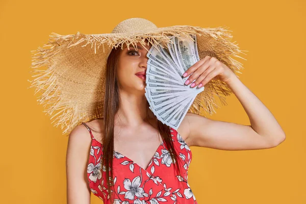 Жінка в літньому солом'яному капелюсі, сукня тримає кусок грошей в руках і позує на жовтому тлі — стокове фото