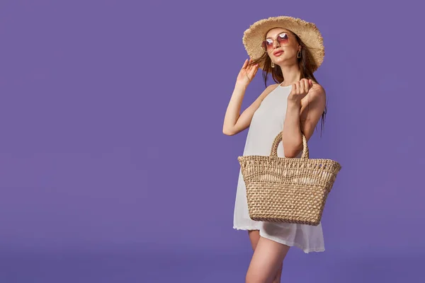 Mulher bonita em vestido branco, chapéu de palha de verão, saco isolado em fundo violeta pastel. — Fotografia de Stock