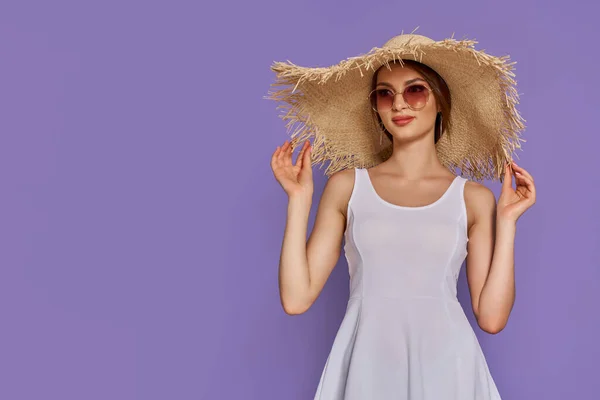Foto de una joven mujer de moda de 20 años que usa vestido con sombrero de paja y gafas de sol aisladas sobre fondo violeta —  Fotos de Stock