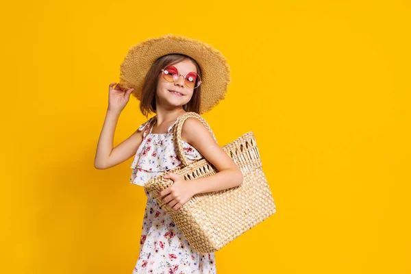 Портрет щасливої веселої дівчини в літньому капелюсі, сонцезахисні окуляри, солом'яний мішок на жовтому тлі . — стокове фото