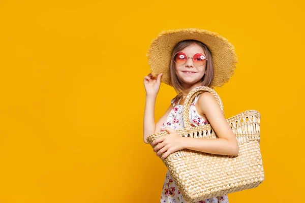 Πορτρέτο του χαρούμενου κοριτσιού σε καλοκαιρινό καπέλο, γυαλιά ηλίου, τσάντα άχυρο πάνω από κίτρινο φόντο. — Φωτογραφία Αρχείου