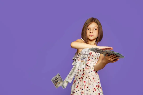 Cheerful and crazy European teenage girl throws money in her hands on a purple background