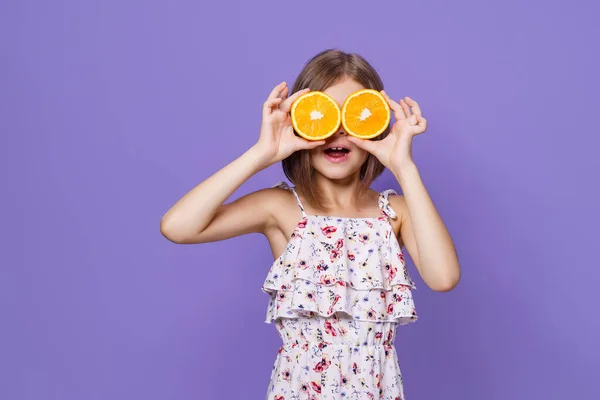 Ευτυχισμένο κοριτσάκι με καλοκαιρινό φόρεμα κρατώντας ένα πορτοκάλι σε κίτρινο φόντο με χώρο για κείμενο. — Φωτογραφία Αρχείου