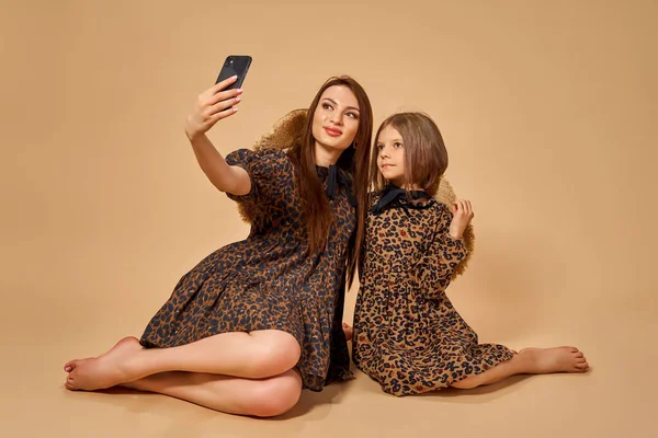 Dos hermosas hermanas jóvenes se toman selfies en bonitos vestidos de patrón animal con sombreros de paja posando en el estudio —  Fotos de Stock