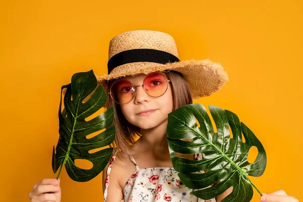 Маленька дівчинка в окулярах і солом'яний капелюх на жовтому фоні в студії — стокове фото
