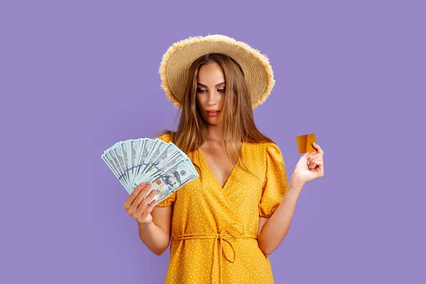 Caucasian woman 20s wearing straw hat holding credit card and fan of dollar cash isolated over purple background — Stock Photo, Image