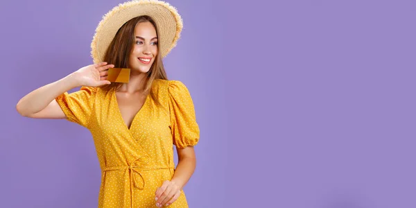 Весела молода кавказька жінка в жовтому одязі і солом "яному капелюсі тримає картку ізольовану на пурпуровому фоні. — стокове фото