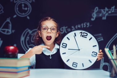 Sınıfın kara tahtasında büyük bir saatle şok olmuş bir öğrenci..
