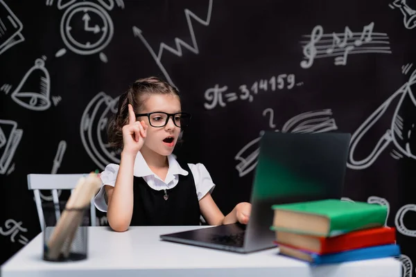 Porträt einer emotionalen Schülerin, die mit erhobenem Zeigefinger denkt und Inspiration oder Lösung findet, mit Laptop am Schreibtisch sitzt und Hausaufgaben macht — Stockfoto