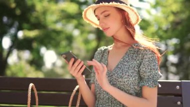 Güzel kızıl saçlı beyaz kız öğrenci akıllı telefon sosyal medya uygulaması kullanıyor. Mesajlaşan gülümseme. Güneşli bahar gününde dışarıda kal.