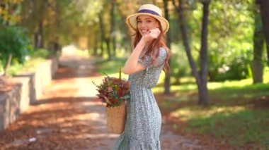 Hasır şapkalı, yaz elbiseli, çiçekli çantalı güzel kızıl kız parkta yürüyor. Yaz zamanı. Sonbahar titreşimleri