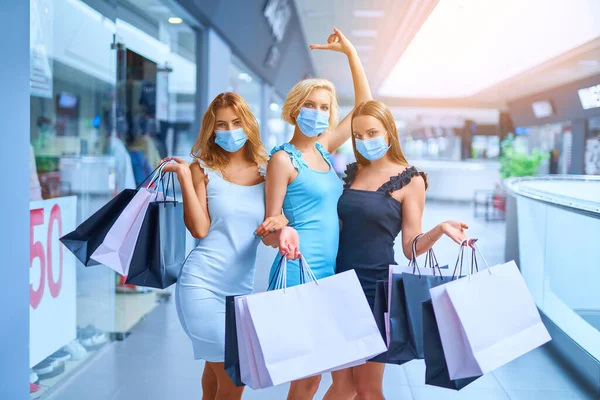 Tres mujeres con estilo en la máscara médica protectora sosteniendo bolsas de compras después de comprar. Compras en la epidemia de coronavirus. Venta, consumismo, Viernes Negro —  Fotos de Stock