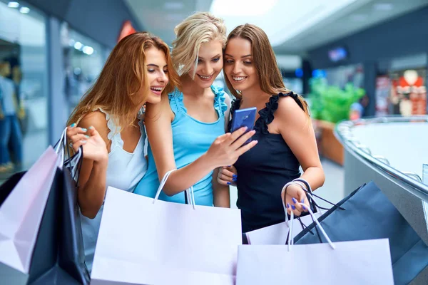 Tres mujer elegante sosteniendo bolsas de compras y mirar en el teléfono móvil después de comprar —  Fotos de Stock