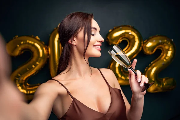 Neujahrsfeier. schöne brünette Frau macht Selfie vor goldenen Luftballons schwarzen Hintergrund 2022. Mit einem Glas Sekt in der Hand. Lächelnd. Champagner trinken — Stockfoto