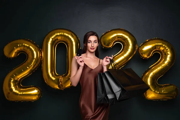 Mulher em vestido elegante segurar cartão de crédito bancário e sacos de compras em fundo preto, números estúdio balões de ar. — Fotografia de Stock
