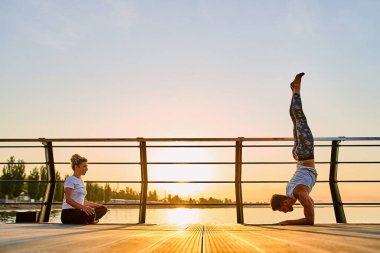 Çift birlikte akrobatik yoga yapıyor, açık denizde doğada amuda kalkıyor..