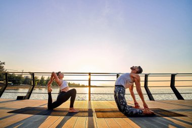Çift açık denizde doğada akrobatik yoga yapıyor..