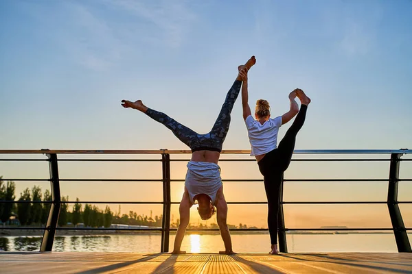 Couple practicing acrobatic handstand yoga together on nature outdoors at sea.
