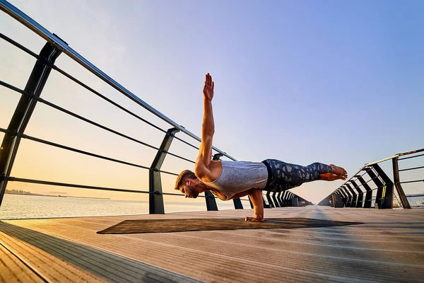 Ajustez l'homme faisant un stand d'une main tout en pratiquant le yoga seul près de l'océan contre le ciel au crépuscule ou à l'aube — Photo