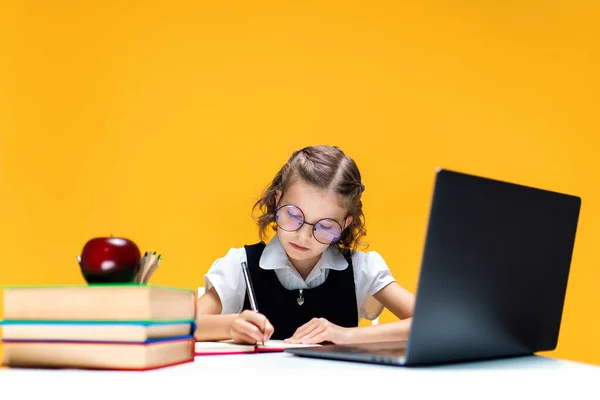 Школярка в окулярах пише і сидить на ноутбуці під час онлайн-уроку. дистанційному навчанні . — стокове фото