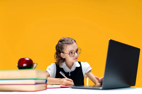 Schulmädchen mit Brille schreibt und sitzt während des Online-Unterrichts am Laptop. Distanziertes Schullernen. — Stockfoto