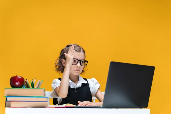 Iskoláslány szemüvegben felemelt kézzel ül a laptopnál az online óra alatt. Távoli iskolai tanulás. — Stock Fotó
