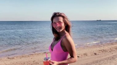 Plajda yürüyen pembe mayolu çekici genç bir kadın.