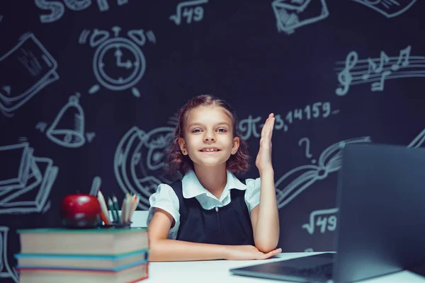 Щаслива школярка піднімає руку, сидячи на ноутбуці під час онлайн-уроку. дистанційному навчанні . — стокове фото
