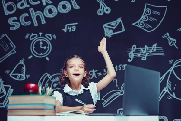 Kavkazská školačka zvedne ruku a během online lekce sedí u laptopu. Vzdálené školní vzdělávání. — Stock fotografie