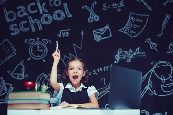 Емоційна школярка піднімає руку ручкою. Сидіти з ноутбуком. Дистанційне навчання — стокове фото