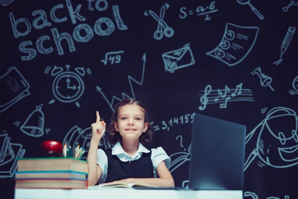 笑顔の女子高生が人差し指を上げた。ノートパソコンや本と一緒に座って。距離教育 — ストック写真