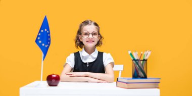 Gülümseyen mutlu beyaz liseli kız İngilizce dersi sırasında masada oturuyor. Avrupa Birliği bayrağı