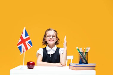 Gülümseyen liseli kız ders sırasında masada oturarak el kaldırıyor. İngilizce dersi. Büyük Britanya bayrağı