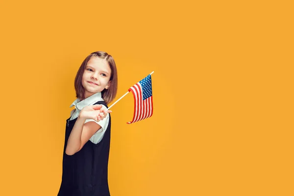 Krásné usmívající se běloška školačka drží americkou vlajku na žlutém pozadí. vlajka USA — Stock fotografie