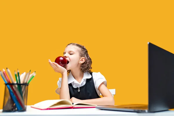 Little schoolgirl eating an apple while change at online lesson. Distance education — Stock Photo, Image