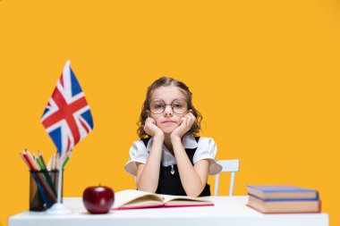 Masada elinde kitaplarla oturan üzgün, sıkıcı, beyaz bir kız öğrenci. İngilizce dersi Büyük Britanya bayrağı
