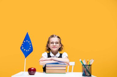 Gülümseyen mutlu beyaz kız masada oturmuş İngilizce dersi Avrupa Birliği bayrağı taşıyor.