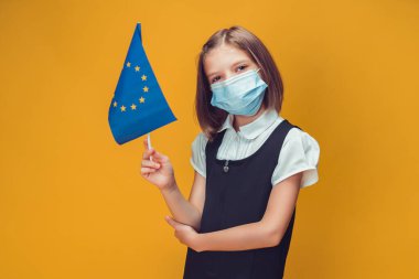 Avrupa Birliği bayrağı taşıyan koruyucu maskeli küçük bir kız öğrenci. Güvenlik kavramı 