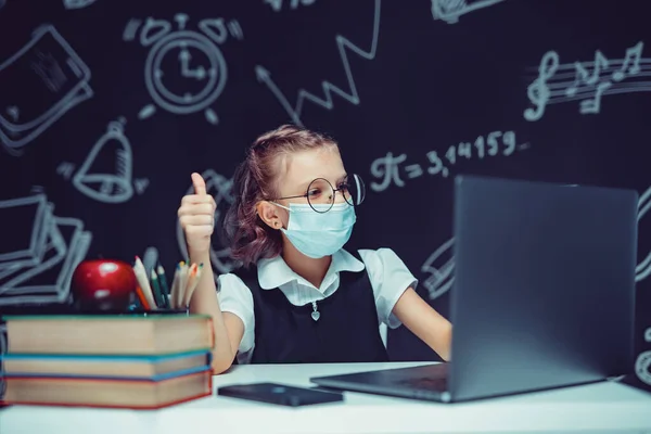 Junior student bär medicinsk mask online virtuell inlärning språk klass på bärbar dator visar tummen upp. — Stockfoto