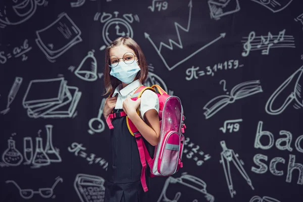 Skolflicka i glasögon i skyddsmask förbereder sig för att gå i skolan. Skydd av barn mot virus — Stockfoto