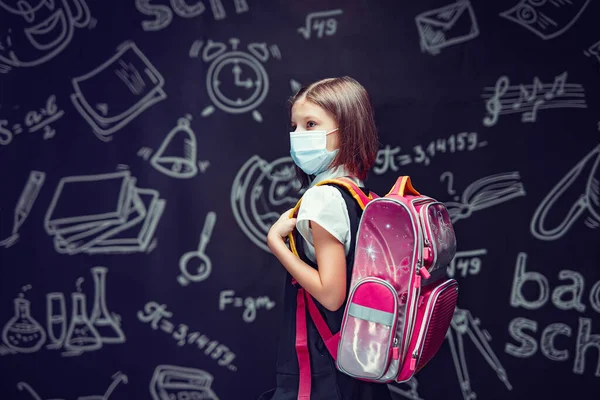 Skolflicka i medicinsk mask förbereder sig för att gå i skolan. Virusskydd för barn. Blickar bort — Stockfoto