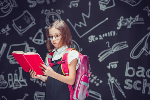 Serieuze leerling in bril die zich voorbereidt om naar school te gaan met een rugzak leesboek. Terug naar school — Stockfoto