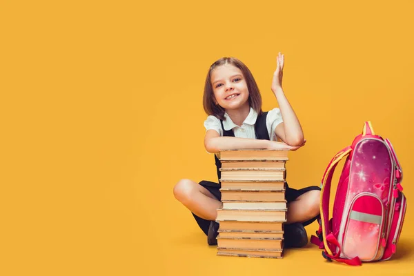 Χαμογελαστή μαθήτρια που κάθεται πίσω από ένα σωρό βιβλία και σηκώνει το χέρι. Έννοια της μάθησης και του σχολείου. — Φωτογραφία Αρχείου