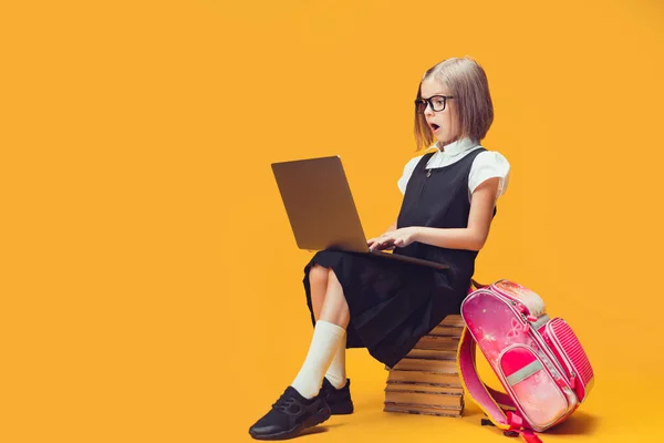 Volledige lengte verraste leerling zittend op de stapel boeken kijkend naar laptop. Onderwijsconcept voor kinderen. — Stockfoto
